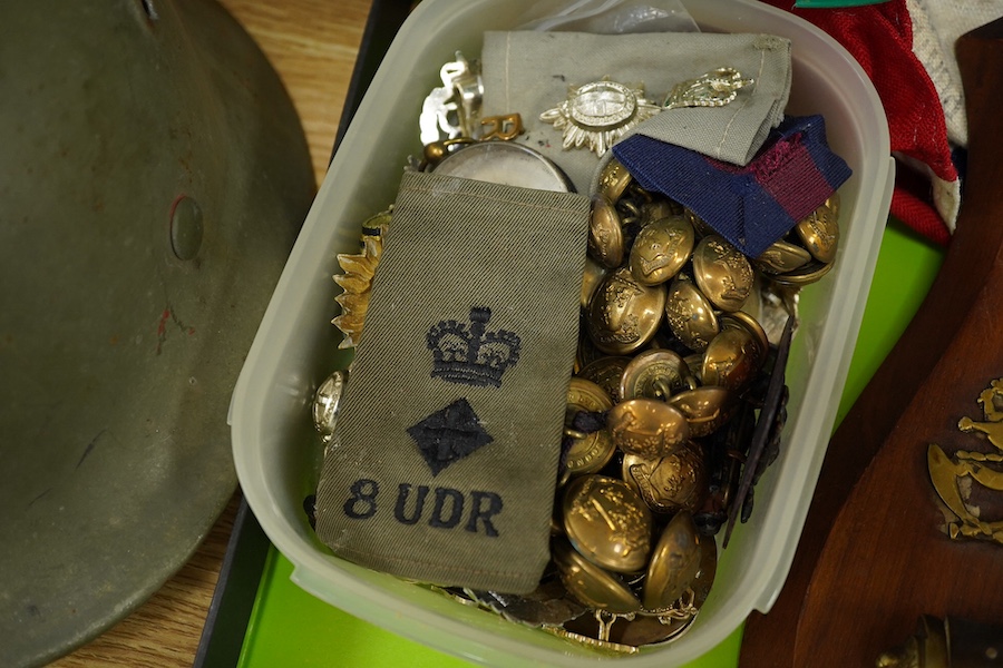 A collection of military items, including a U.S. Army helmet, an M42 helmet, a WWII British Home Front helmet, a Union flag 96cm x 60cm, a compass, a Kukri display shield, and a box of military cap badges, buttons, etc.